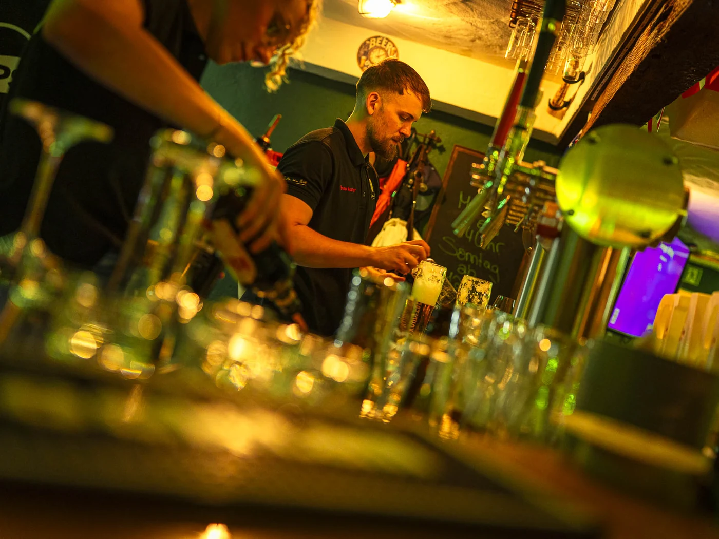 Mitarbeitende hinter der Theke im Shamrock Pub beim Zapfen und Zubereiten von Getränken.